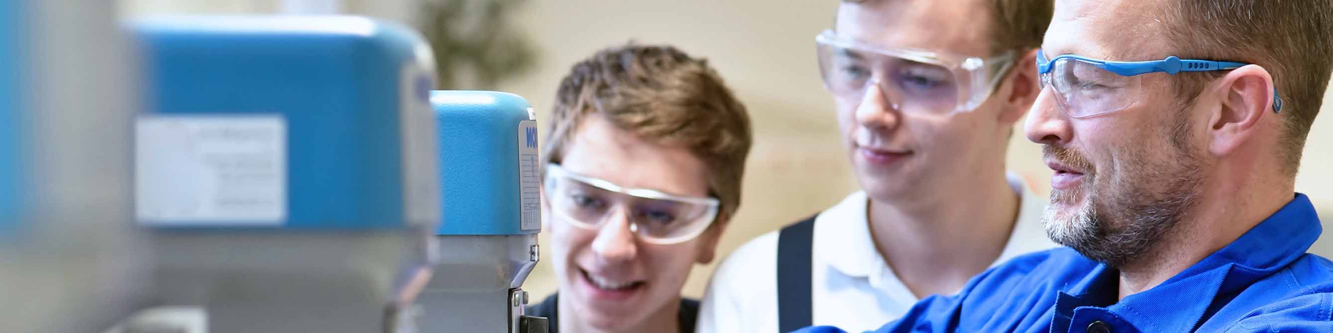 Anlagenleiter zeigt zwei Praktikanten die Bedienung einer Maschine.
