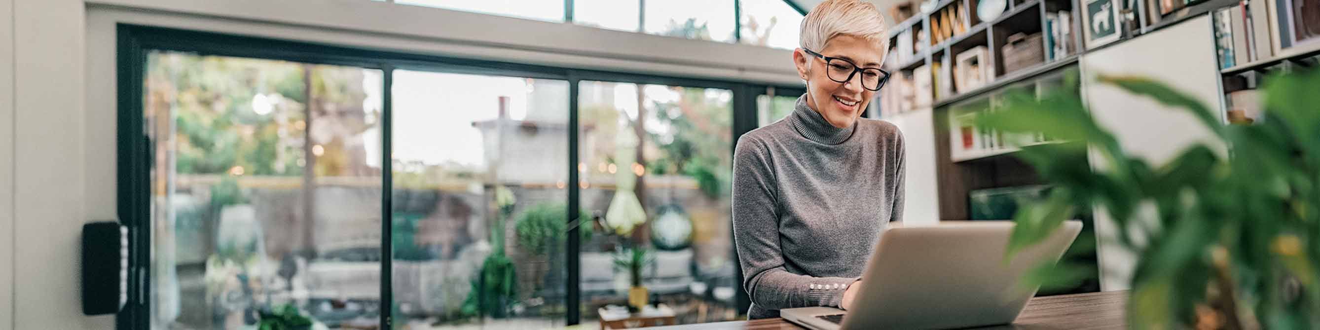 Frau mit dunkler Brille und kurzen weißen Haaren sitzt vor einem Laptop  