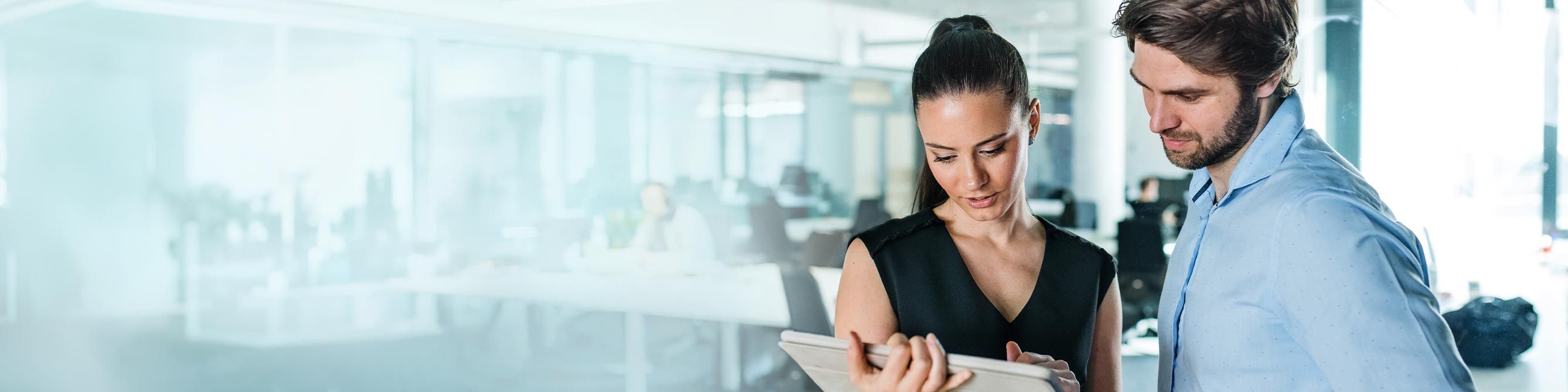 Ein Mann und eine Frau stehen in einem Büro beiden schauen auf einen Tablet-PC