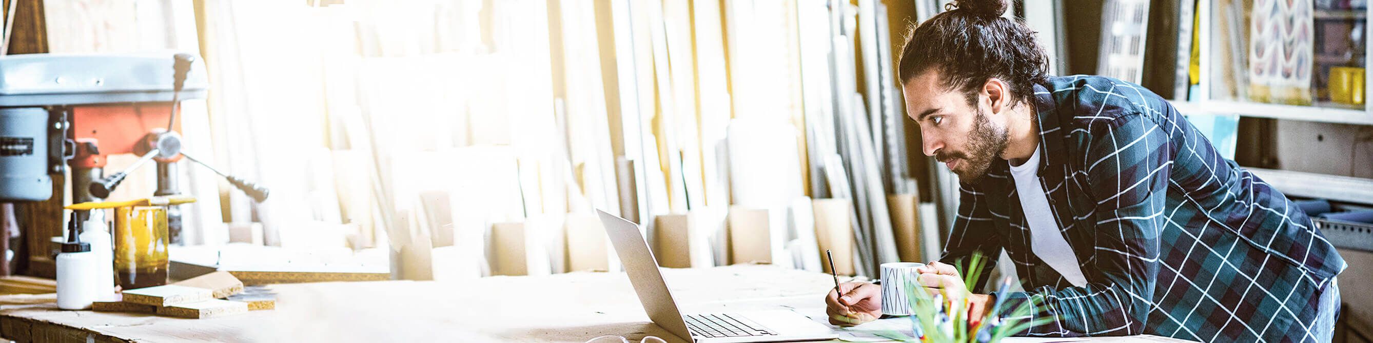 Firmenkunde in seiner Werkstatt liest am Laptop Informationen zu Versicherungen für Handwerksbetriebe