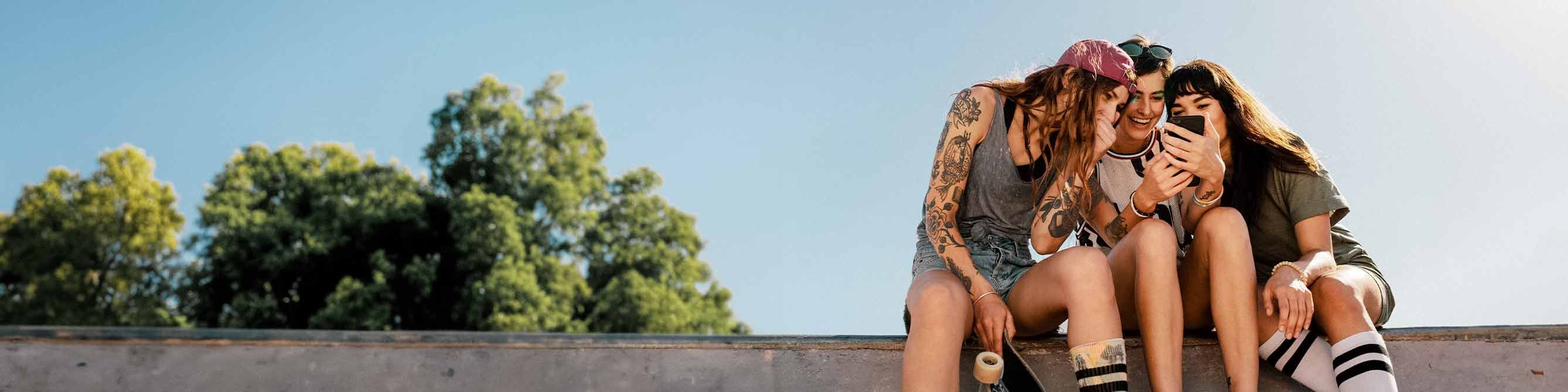 Drei Frauen an einer Skaterrampe schauen auf ein Smartphone