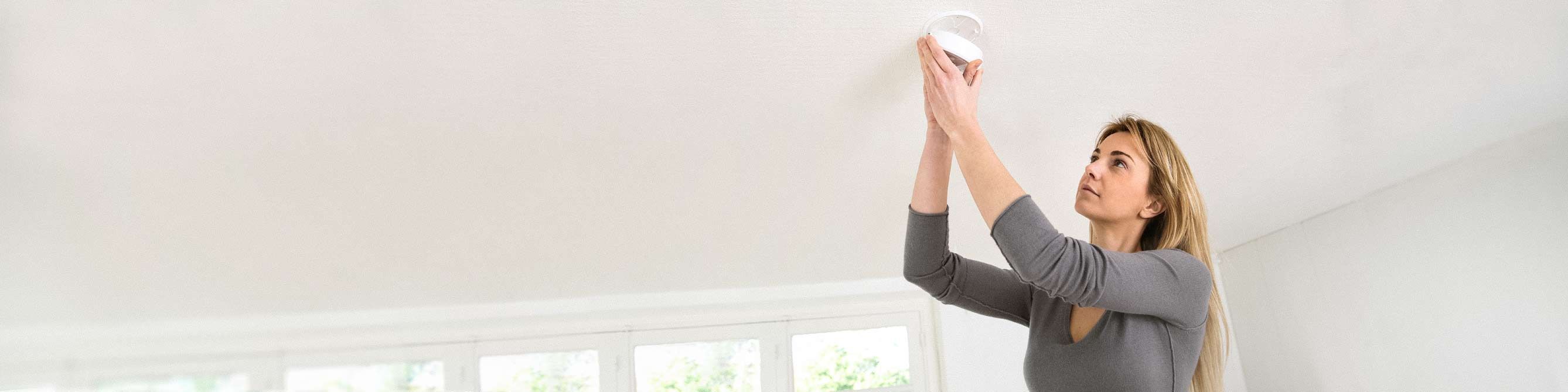 Frau bringt Rauchwarnmelder unter der Decke an