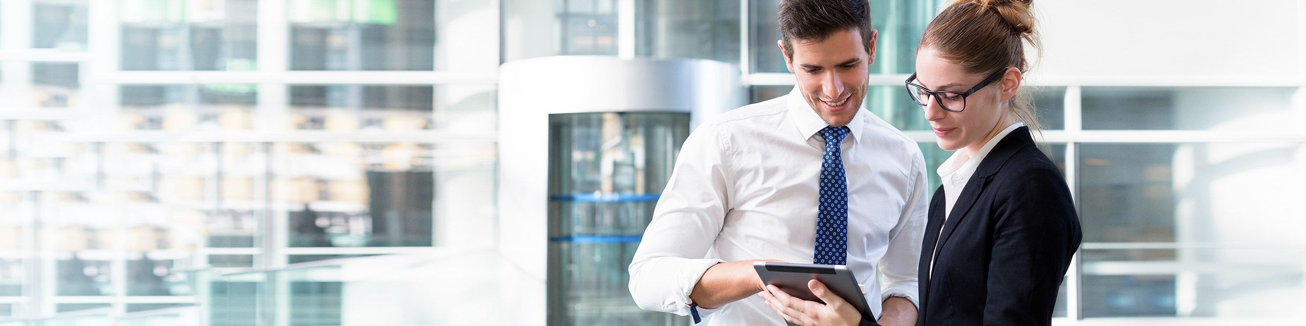 Ein Mann und eine Frau stehen in einem Büro und schauen beide auf ein Tablet.