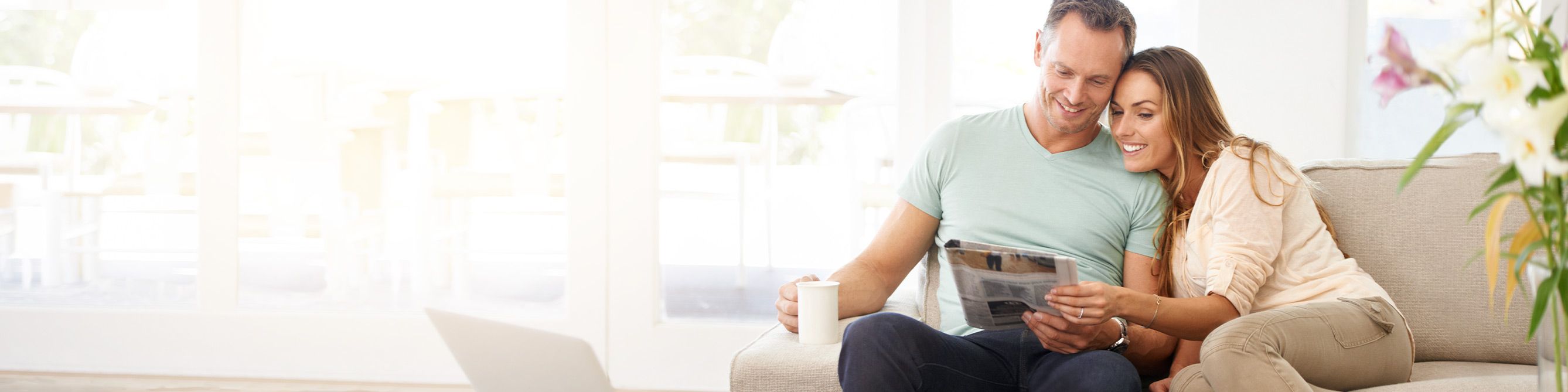 Ein junger Mann und eine junge Frau sitzen auf einem Sofa und schauen beide in einen Prospekt.
