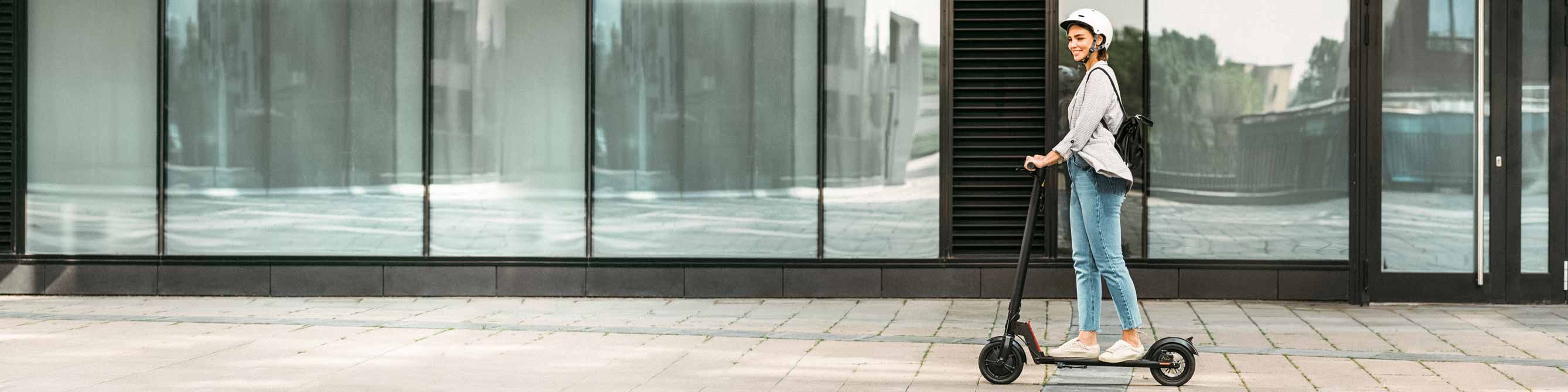 Frau fährt mit E-Scooter vor einer Fensterfront 