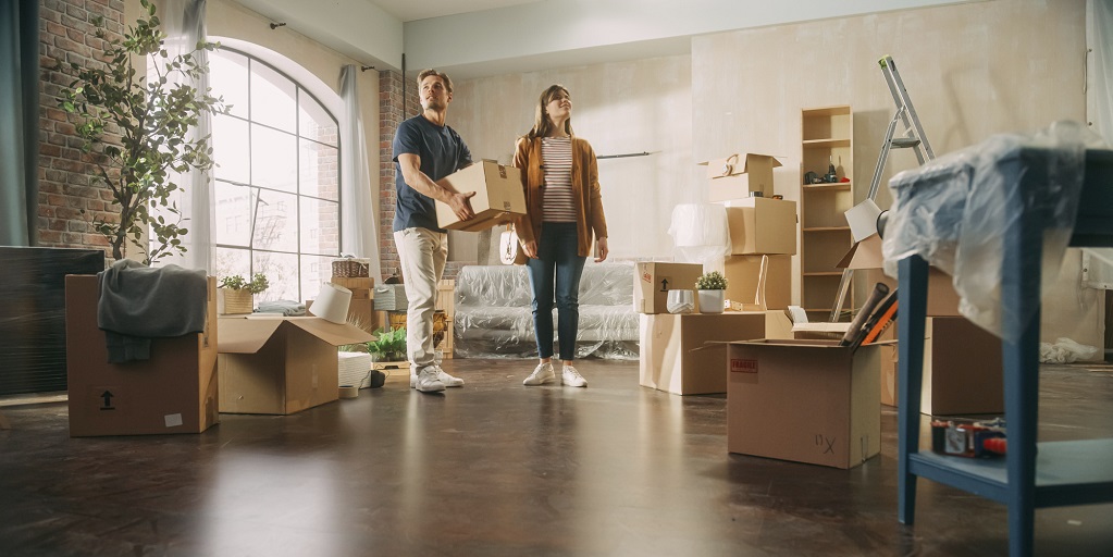 Ein junges Paar steht in einer leeren Wohnung umgeben von Umzugskartons.