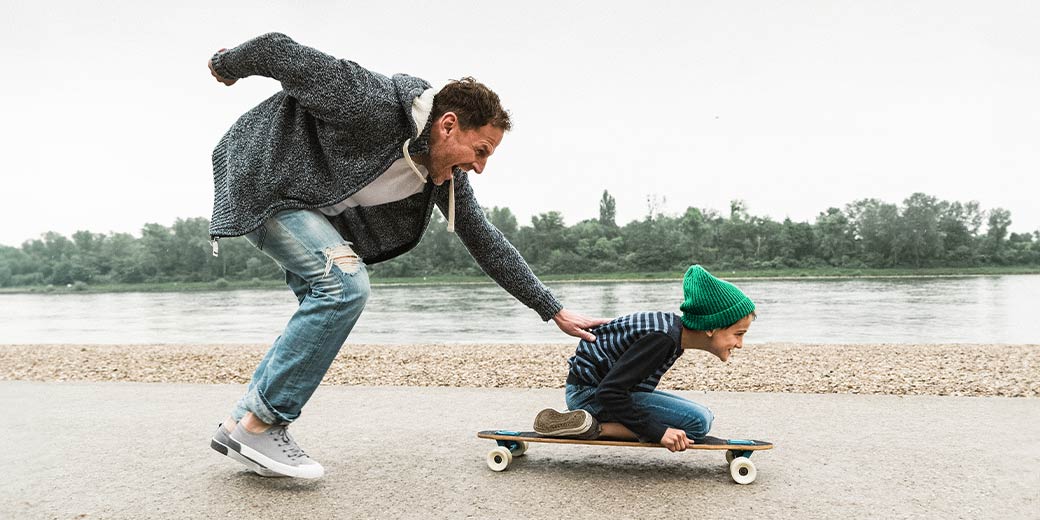 Vater schiebt Sohn auf Skateboard an