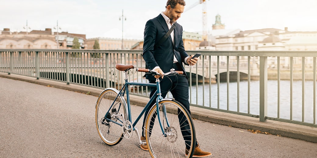 Mann schiebt sein Fahrrad und schaut dabei auf sein Smartphone