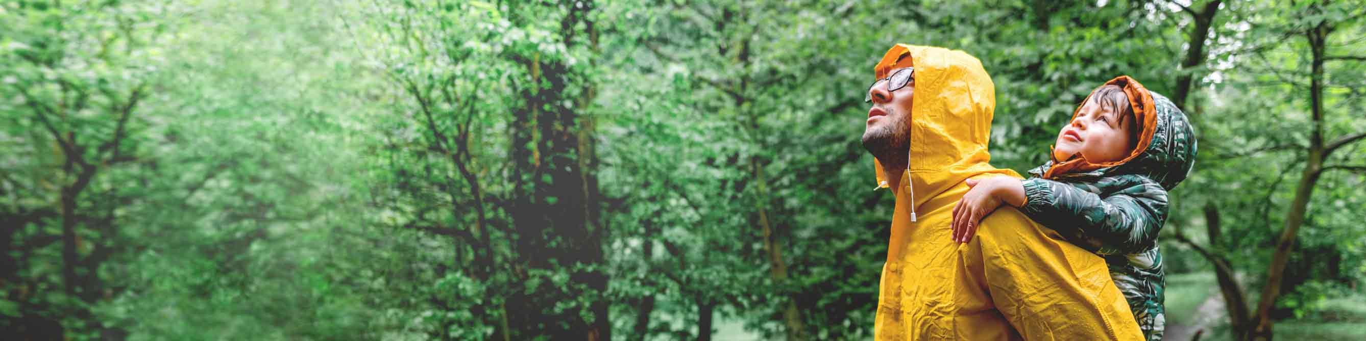 Mann mit Kind auf dem Rücken im Wald bei Regen