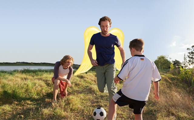 Private Haftpflichtversicherung: Vater spielt mit seinen Söhnen im Garten Fußball. Der Vater hat Schutzengel-Flügel.