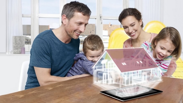 Hausratversicherung: Eine Familie sitzt am Esstisch, auf dem das Hologramm eines Hauses eingeblendet ist.